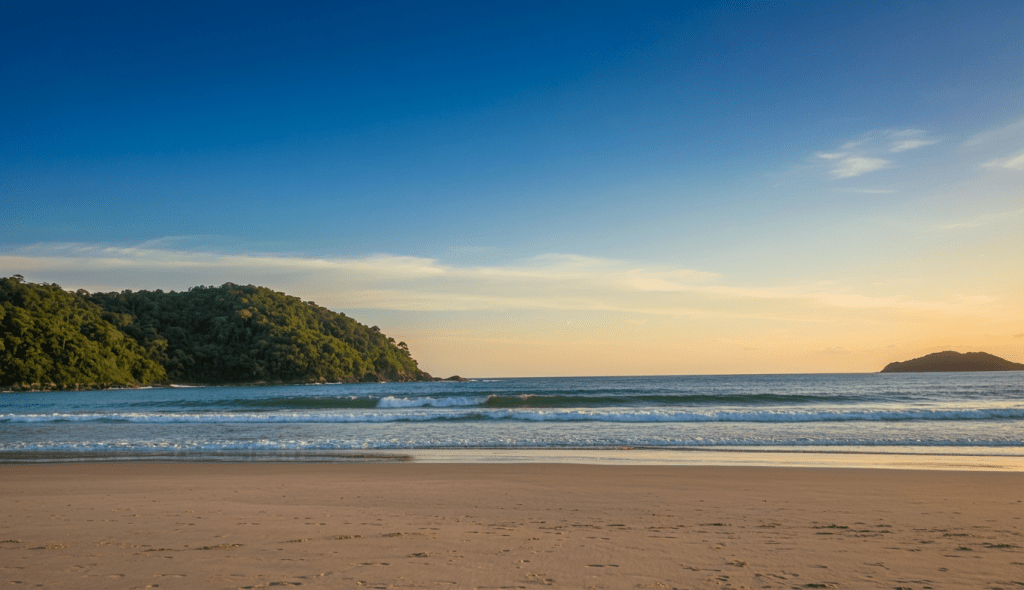 Fotografia artística de uma praia em Florianópolis ao entardecer, com mar calmo, céu em tons de azul e dourado, vegetação da Mata Atlântica ao fundo e clima de refúgio acolhedor e sereno
